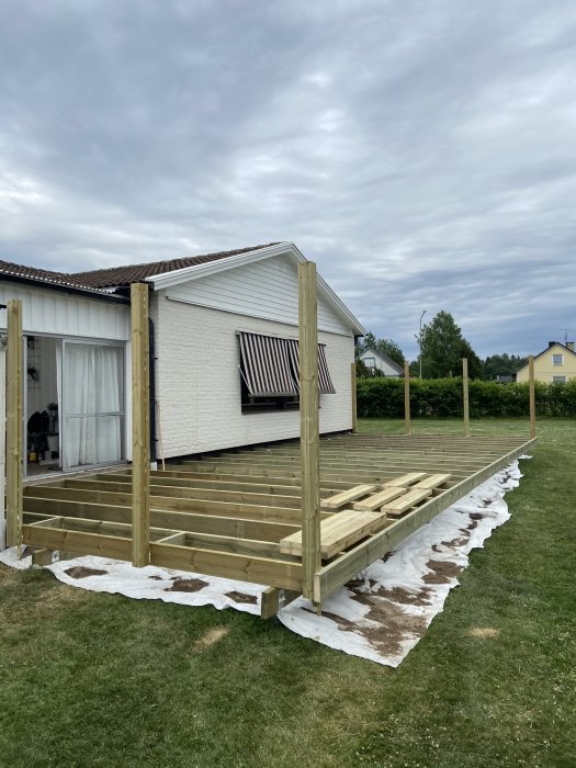 Nybyggd trätrall utan räcken vid ett vitt hus med grå himmel i bakgrunden.