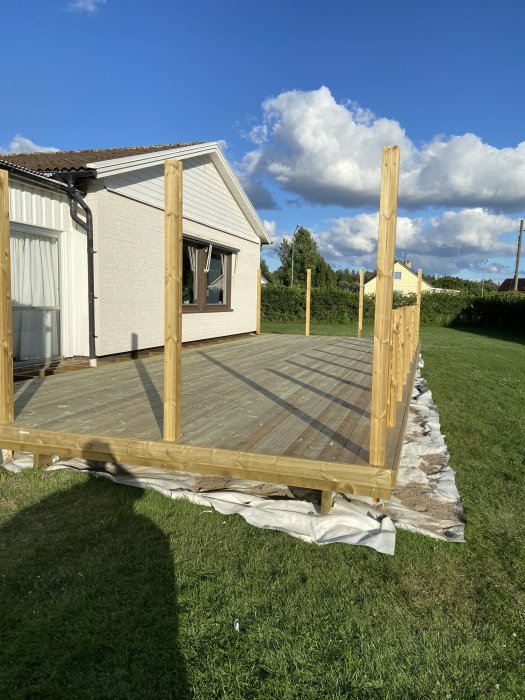 Nybyggd trätrall utan räcken framför ett hus med blå himmel i bakgrunden.