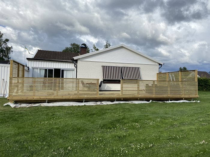 Nybyggd träaltan med räcken framför ett hus, redo att användas.