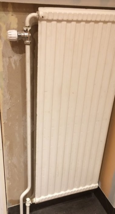 Väggmonterad radiator med stängd ventil och underliggande anslutningsrör i ett målningsprojekt.