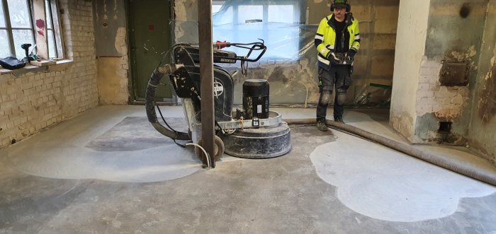 Arbetare slipar betonggolv med slipmaskin, visar slätad yta efter ett poleringssteg med grit 150.