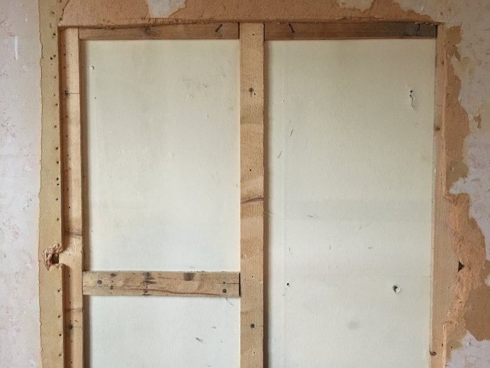Renoverad vägg med avlägsnad tapet visar träreglar och en exponerad spånskiva på en yttervägg i ett äldre hus.