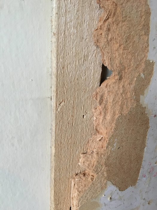 Närbild på en delvis riven spånskivsvägg med synliga träfibrer och rester av tapet.