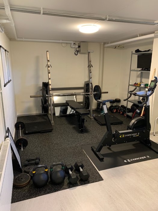 Välorganiserat hemmagym med skivstångsställning, roddmaskin, hantlar och kettlebells.