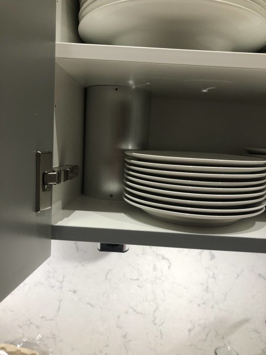 Öppet köksskåp med en stapel mindre tallrikar bredvid en rund behållare, begränsat med utrymme.