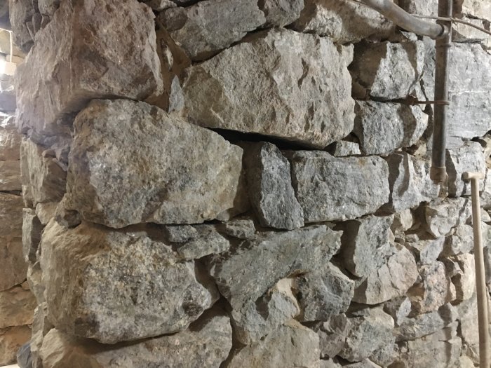 Stentextur av en vägg under renovering med sprängsten som omfogas, synliga murslev och byggmaterial.