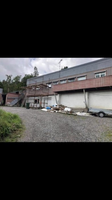 Renoverad byggnad med oavslutad balkong och byggnadsavfall framför.