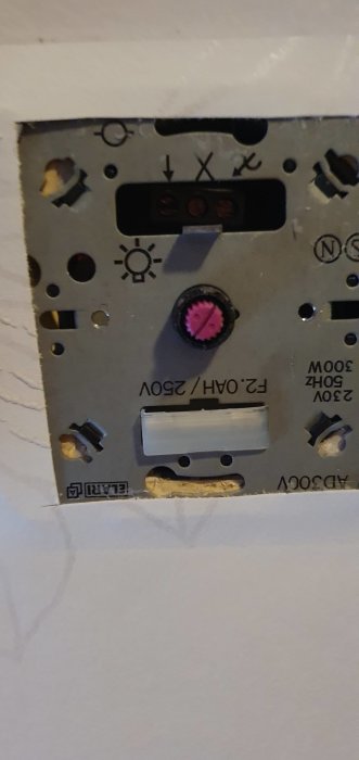 Öppen elektrisk dimmerutrustning i vägg med synlig rosa säkring och kabelförbindelser.