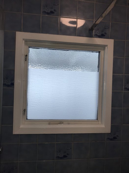 Nyinstallerat frostglasfönster i renoverat badrum med kaklade väggar.