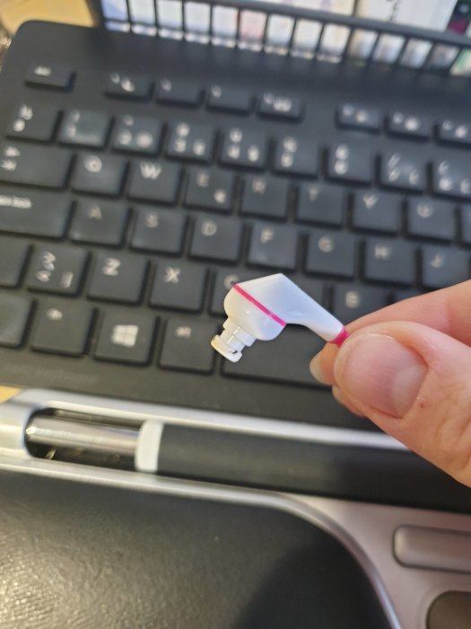 En hand håller en vit och rosa USB-laddare framför ett tangentbord.