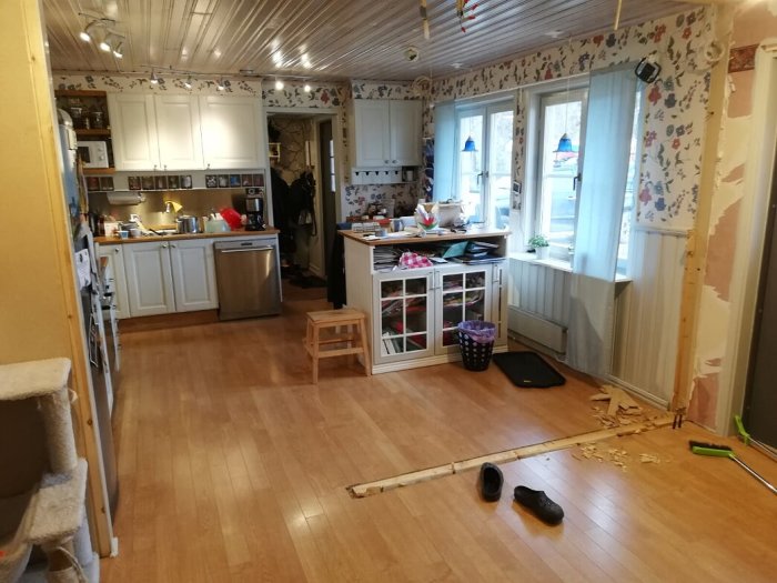 Kök under renovering med riven vägg, golv och köksskåp synliga samt verktyg på golvet.