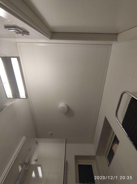 Vy uppåt i ett badrum visar ett vitt trätak med en central glödlampa, kaklade väggar och en del av en duschdörr.
