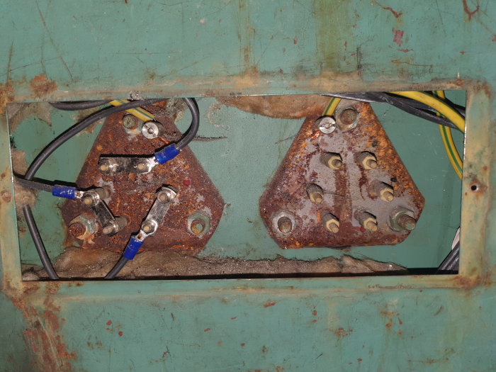 Rostiga säkringspatronhållare med ojämnt fördelade kablar inuti ett elskåp.