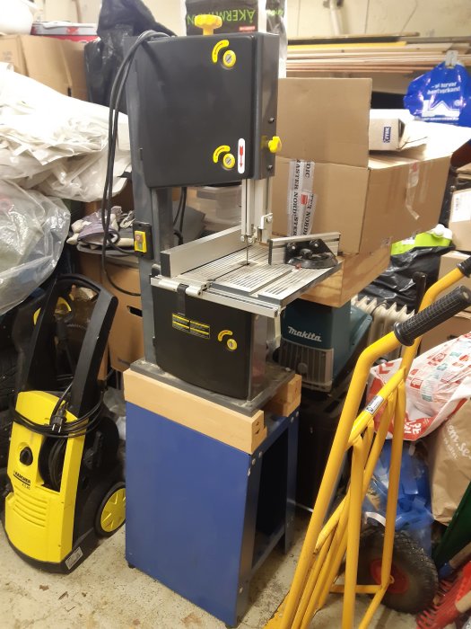 Begagnad cotechbandsåg på blått ställ i rörigt garage med verktyg och lådor i bakgrunden.