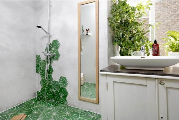 Badrum med grön kaklad dusch, träpall, handfat, spegel och växtdekoration.