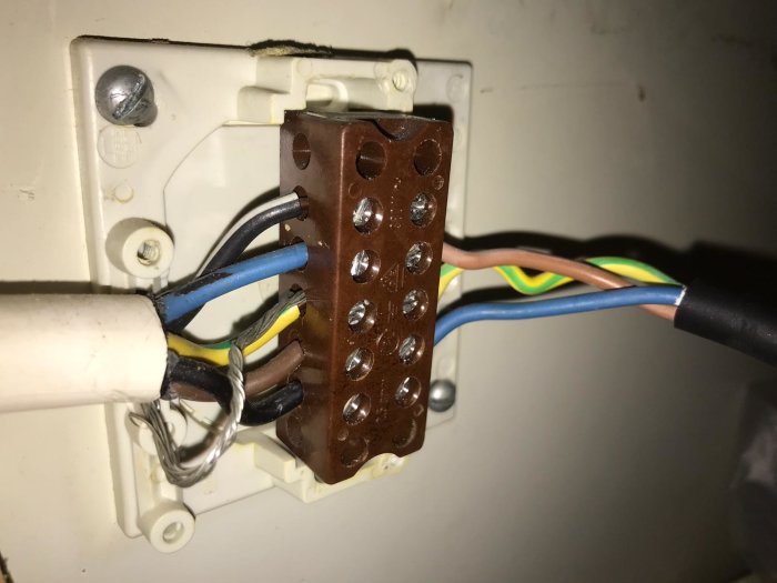 Elkablar kopplade till en brun anslutningsplint bakom en vit apparat.