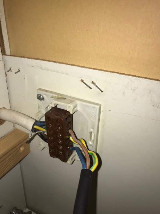Elkablar inkopplade i en vägguttag bakom en vit apparat, synliga färgade ledare och termineringsblock.