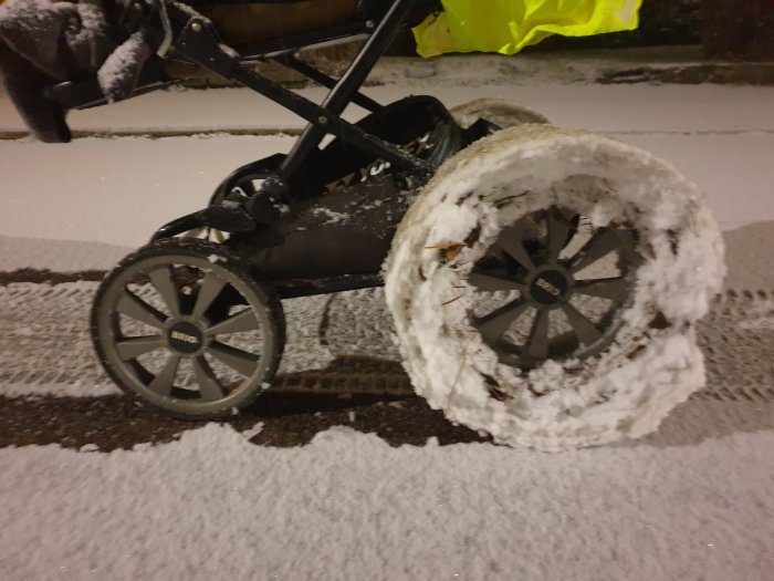 Barnvagn med snötäckt hjul på en snöklädd väg under kvällen.