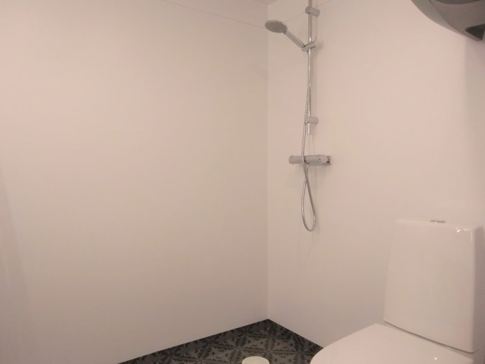 Delvis renoverat badrum med dusch och toalett i drift, varmvattenberedare delvis synlig.