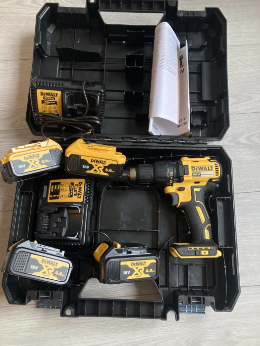 Öppen verktygslåda med Dewalt skruvdragare, fyra batterier och två laddare på ett golv.