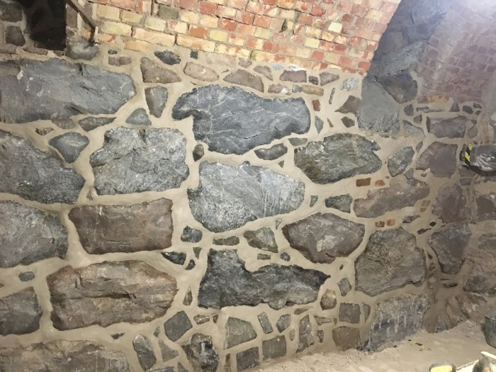 Fogad stenmur med varierande storlek av stenblock och ny fogmassa, några tegelstenar synliga.