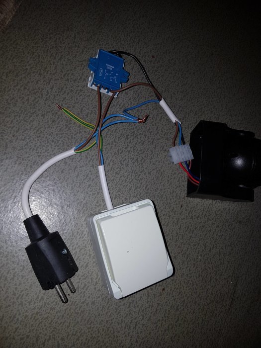 Elinstallation med stickpropp, kopplingsdosa, rörelsevakt och vägguttag på golv.
