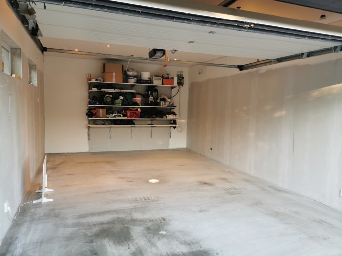 Renoverat garage med spacklade väggar, vita takskivor och plats för skjutdörrar och förvaring.