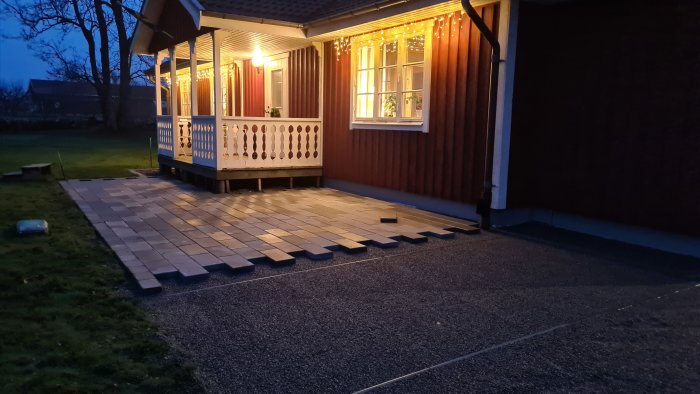 Exteriör av ett hus vid skymning med nyinstallerade plattor längs grunden och belysning i fönster och under tak.