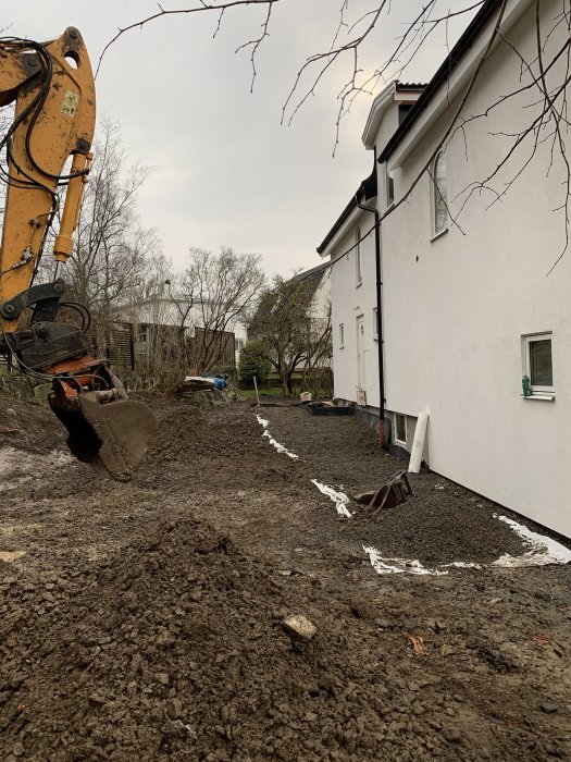 Äldre hus under renovering med grävmaskin och byggarbetsplats i trädgården.