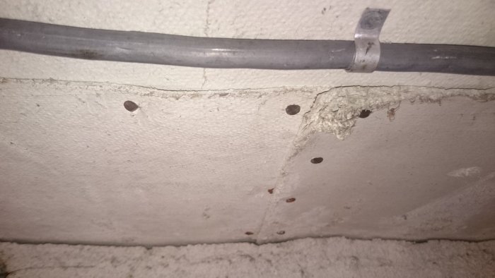 Elledning fästad på en betongvägg med klamrar, väggen har borrade hål och en skadad del.