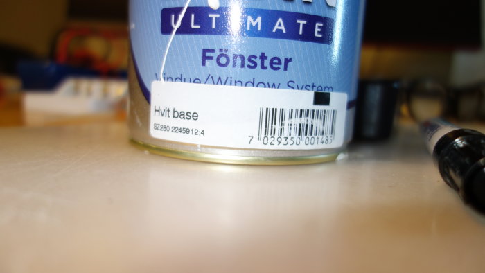 Burk med Jotuns fönsterfärg i vitt med etiketten "ULTIMATE Fönster" på en arbetsbänk.