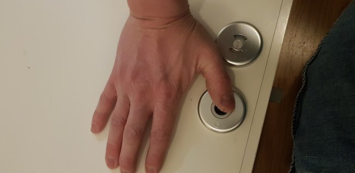 Hand som försöker vrida ett trögt badrumsdörrslås, visar problemet beskrivet i inlägget.