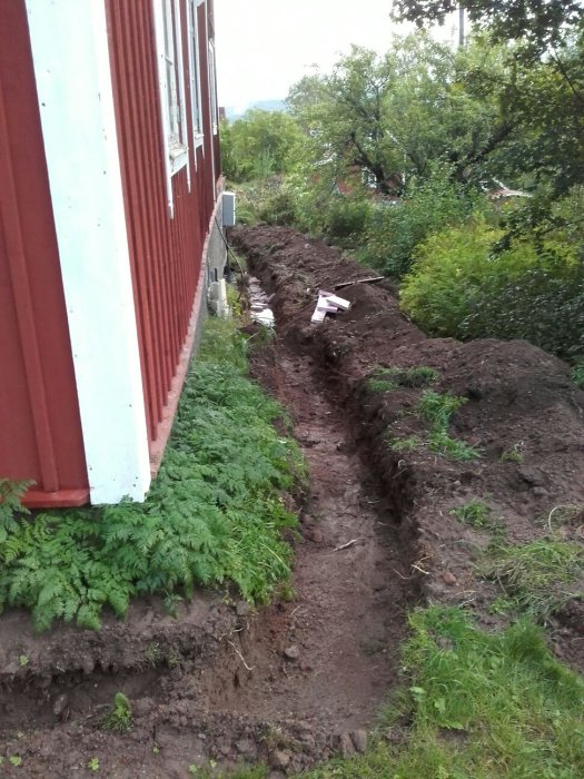 Uppgrävd grävning längs en byggnads sida för reparation av en skadad elkabel.