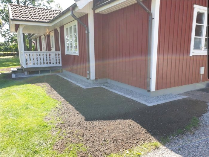 Rensat område runt rött trähus med veranda, nygrusad gång och markerad grund.