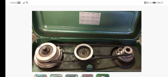 Svart rem monterad på rullar inne i en öppen grön väska med metallskivor och borrstorlekstabell på insidan av locket.