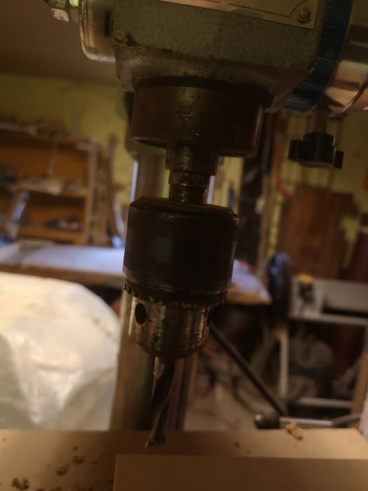Närbild av en borrchuck på en pelarborrmaskin med borrbiten ovanför ett arbetsstycke.
