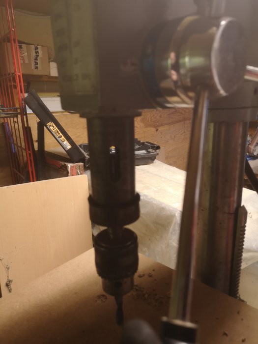 Närbild av borrchuck på pelarborrmaskin med borrinsats och trästycke under beredning.