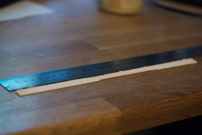 Noggrant uppmätt glasspinne sågad till 1,5 mm tjocklek ligger på ett träbord med en linjal ovanpå.