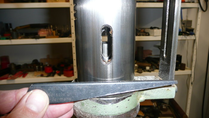 En hand håller ett metallverktyg nära slitsen i en stor metallpinol med en verkstadsbakgrund.