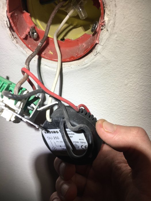 En hand håller en Schneider elektrisk dimmer med anslutna kablar i en öppen vägguttag.