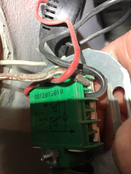 Närbild på en grön Schneider elektrisk komponent med röd och vit kabel ansluten, samt verktyg i bakgrunden.