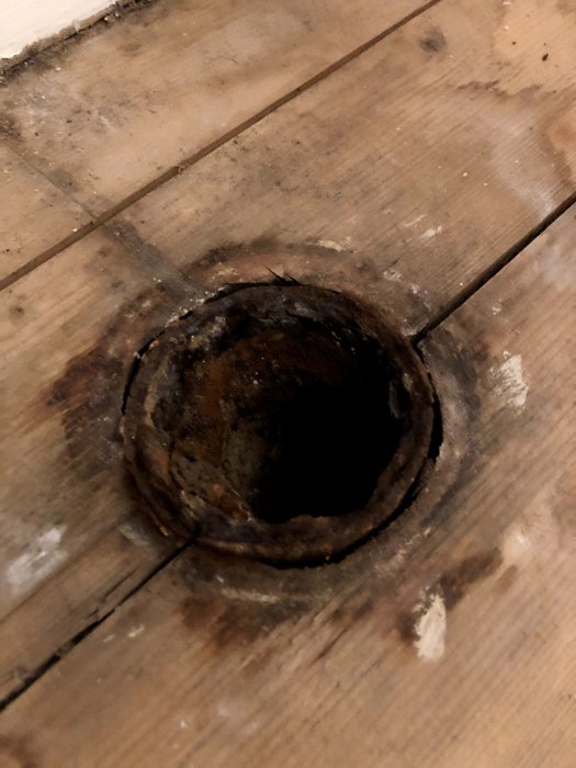 Gamla skadade rör i trägolv genom vilka vatten läckt från övervåningen.