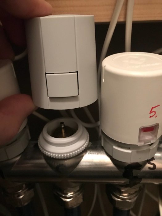 Hand som håller en vit termostat nära monteringsplats på ett radiatorrör.