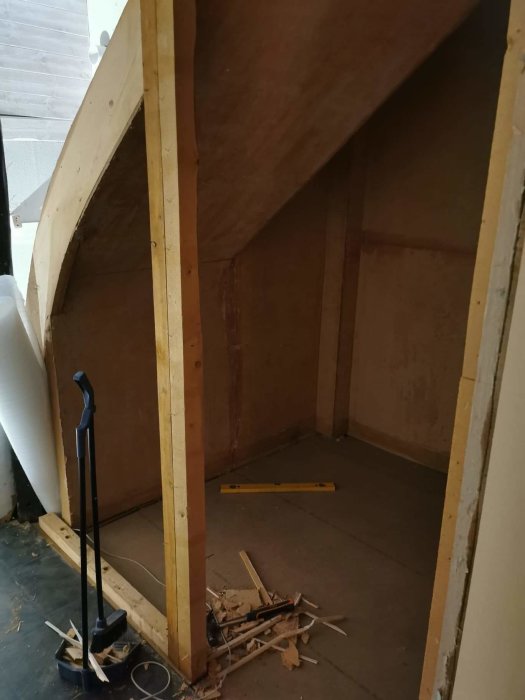 Nybyggd garderob under trappa med synligt regelverk och byggavfall.