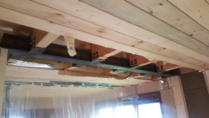 Wooden ceiling beams with metal brackets; insulation material visible. Discussion about modifications on beam widths and construction adjustments.