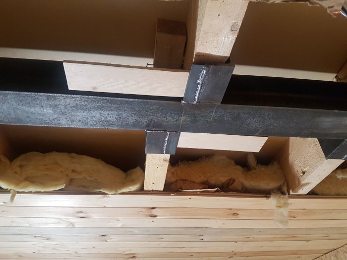 Wood beams and insulation in a ceiling with a metal support beam.