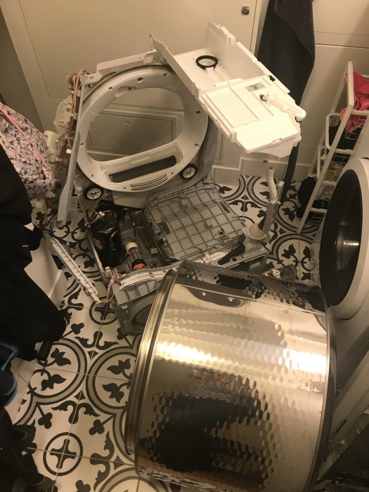 Nedmonterad torktumlare med delar och trumma synliga på ett mönstrat golv.