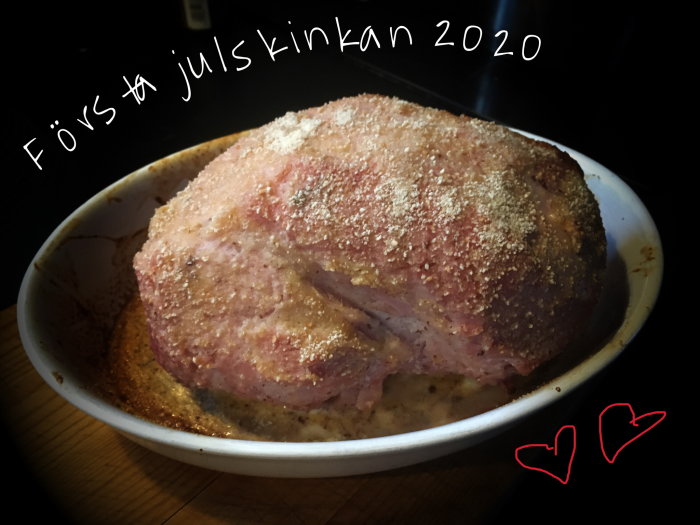 Ogrillad julskinka i en ugnsform med texten "Första julskinkan 2020" och hjärtsymboler.