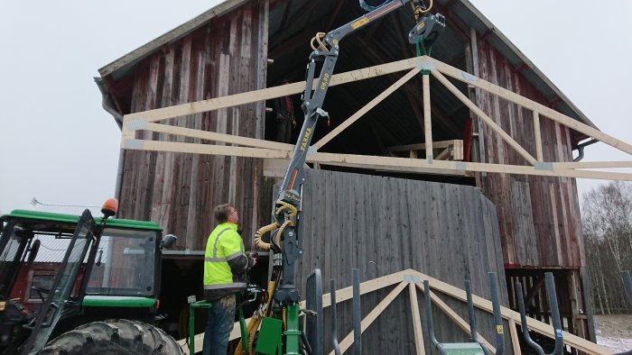 Installation av en färdig takstol på en byggnad med hjälp av lyftanordning och traktor.