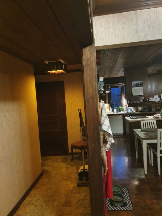 Talo sisältä, käytävä ja yhdistetty olohuone-keittiötila, puolikas seinä erottamassa, huonekaluja ja mattoja näkyvissä.